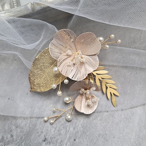 May include: A gold floral hair comb with two blush pink flowers, gold leaves, and pearl accents.