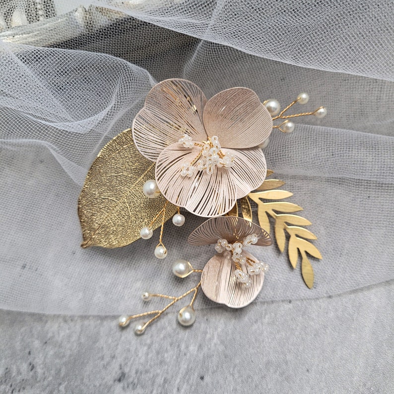 May include: A gold floral hair comb with two blush pink flowers, gold leaves, and pearl accents.
