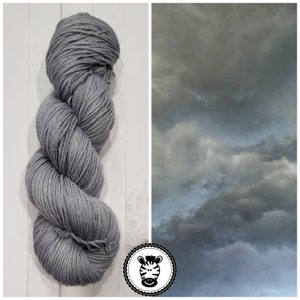 May include: A skein of light gray yarn with a subtle sheen. The yarn is wound into a ball shape and is ready for knitting or crocheting.