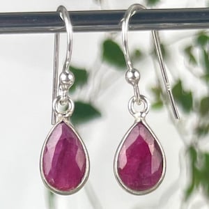 May include: Sterling silver drop earrings with pear-shaped, faceted ruby gemstones. The rubies are a deep red colour and set in a bezel setting. The earrings have a simple, elegant design, suitable for everyday wear or special occasions.