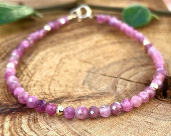 May include: A delicate bracelet made with small, faceted pink gemstones and gold beads. The bracelet is strung on a thin gold chain.