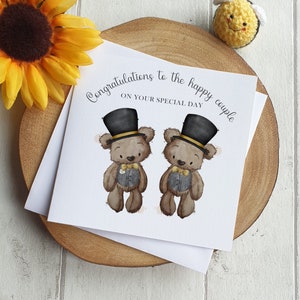 May include: A wedding card with the message "Congratulations to the happy couple ON YOUR SPECIAL DAY." The card shows two teddy bears in top hats and bow ties. It rests on a wooden slice, with a sunflower and a crocheted bee nearby.