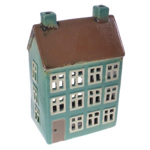 Könnte beinhalten: Ein tealfarbenes Keramikhaus mit braunem Dach und mehreren Fenstern. Das Haus hat eine kleine Tür und ist für Teelichter konzipiert.