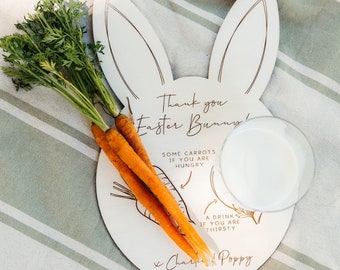 Peut inclure: Assiette en bois blanc en forme de lapin avec le texte "Merci au lapin de Pâques !" et des illustrations de carottes et d'un verre de lait. Le texte "Quelques carottes si vous avez faim" et "Une boisson si vous avez soif" est écrit sous les illustrations. L'assiette est signée "x Charlie & Poppy".
