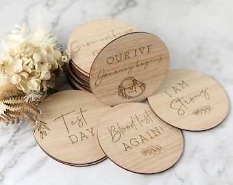 May include: Wooden circle ornaments with text that reads "Our IVF Journey Begins", "Test Day", "Blood Test Again", and "I Am Strong".