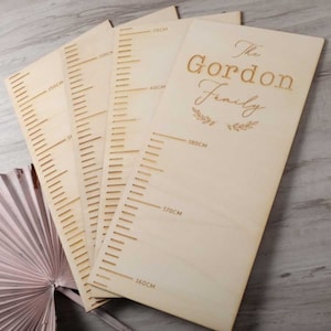 Könnte beinhalten: Ein Satz aus vier Holz-Wachstumstabellen mit einer personalisierten Inschrift, die "The Gordon Family" lautet. Die Tabellen zeigen Messungen in Zentimetern von 60 cm bis 180 cm.