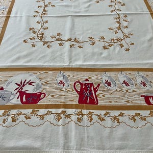 May include: A vintage white tablecloth with a brown wood grain border and decorative elements. The tablecloth features red and gray teacups, teapots, and plates. Brown vines and leaves are printed on the white background.