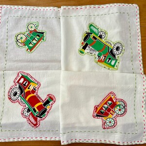 May include: Four white cotton tea towels with green, red, and yellow embroidered train designs. The trains are all different styles and have different colored wheels.