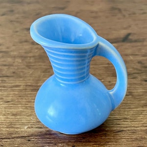 May include: A small, light blue ceramic pitcher with a ribbed design and a handle. The pitcher is about 4 inches tall.