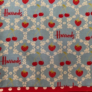 May include: A blue fabric with a white pattern of swirls and cherries. The fabric has the word "Harrods" repeated in red.