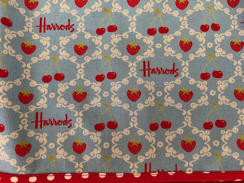 May include: A blue fabric with a white pattern of swirls and cherries. The fabric has the word "Harrods" repeated in red.