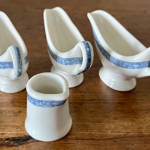 May include: Four white ceramic sauce boats with blue and white floral designs. The boats are arranged in a row on a wooden surface.