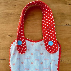 May include: Red and white polka dot bib with blue buttons. The bib has a light blue background with a strawberry pattern.