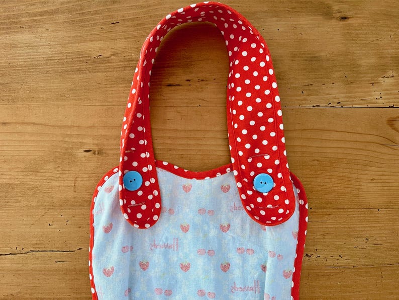 May include: Red and white polka dot bib with blue buttons. The bib has a light blue background with a strawberry pattern.
