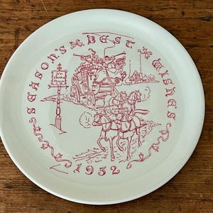 May include: A white ceramic plate with a red illustration of a horse-drawn carriage and the text "Season's Best Wishes" and "1952". The plate has a decorative border and is likely a vintage collectible.