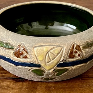 May include: A ceramic bowl with a green glaze inside and a gray exterior. The bowl is decorated with a geometric pattern in shades of brown, green, blue, and yellow.