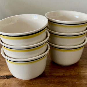 May include: Six white ceramic bowls with yellow and black stripes. The bowls are stacked in a pyramid shape.
