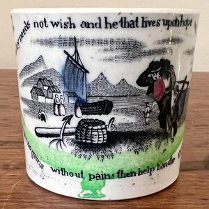 May include: A white ceramic mug with a black and white illustration of a boat, a man, and a woman. The mug has green and blue accents and the text "by needs not wish and he that lives uponhope without pains then help hander" printed on it.