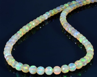 May include: A necklace featuring faceted opal beads. The beads are mainly white, with iridescent flashes of green, yellow, and orange. The necklace is set against a dark blue backdrop, accentuating the gemstones' brilliance.