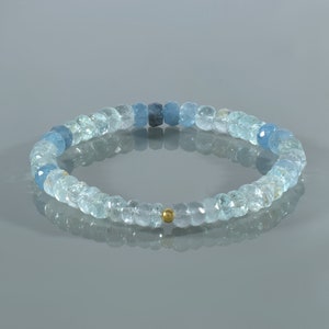 May include: A light blue aquamarine gemstone bracelet with a gold bead accent. The bracelet is made of faceted beads and is strung on elastic.