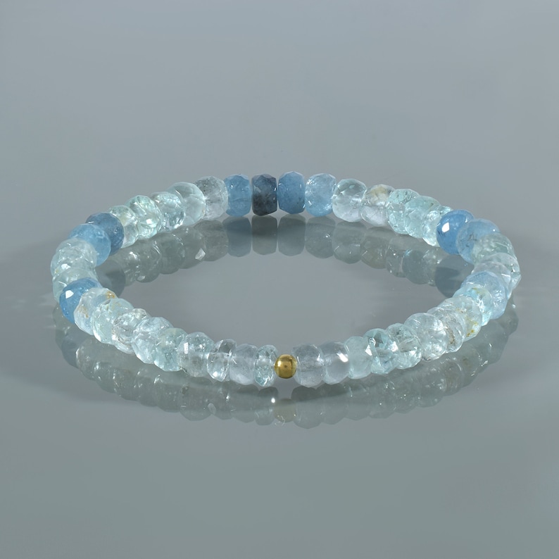 May include: A light blue aquamarine gemstone bracelet with a gold bead accent. The bracelet is made of faceted beads and is strung on elastic.