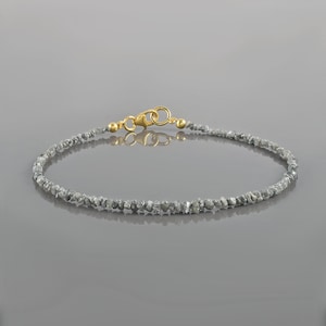 Puede incluir: Un delicado brazalete hecho con una hebra de pequeños diamantes en bruto grises. El brazalete tiene un cierre de oro.