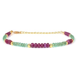 Puede incluir: Un brazalete de cadena dorada con cuentas de piedras preciosas verdes y rojas alternas.