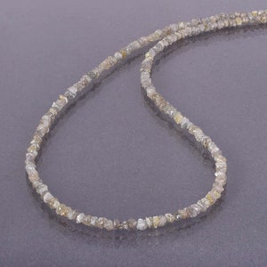 May include: A strand of rough, unpolished, gray diamonds strung together on a thin thread, forming a necklace.