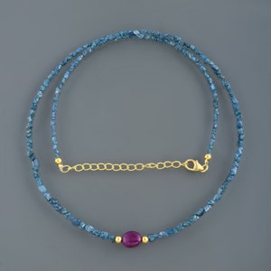 May include: A delicate necklace made with blue rough diamonds and a single ruby gemstone. The necklace has a gold chain extender.