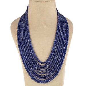 Può includere: Una collana a più fili composta da numerose piccole perline blu scuro sfaccettate. La collana è drappeggiata su un busto di manichino, mettendo in risalto il suo design a strati e il suo colore intenso. Le perline sembrano essere di dimensioni e forma uniformi.