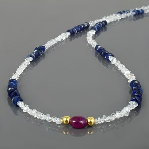 Könnte beinhalten: Eine Halskette aus weißen und blauen Edelsteinperlen mit einer einzigen roten Edelsteinperle in der Mitte.