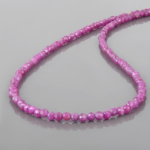 Pode incluir: Um colar de pedras preciosas de rubi rosa com contas facetadas. O colar é feito de pequenas contas redondas que são enfiadas em uma corrente fina.
