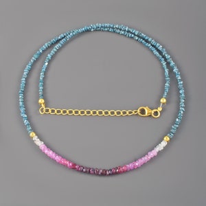 Könnte beinhalten: Eine Perlenkette mit einem langen Strang aus kleinen, rauen blauen Steinen, die in einen Abschnitt aus facettierten rosa und magentafarbenen Perlen übergehen. Die Kette verfügt über eine goldfarbene Metallverlängerung und einen Karabinerverschluss.