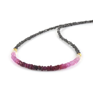 May include: A delicate necklace featuring a gradient of pink and red gemstones, interspersed with black diamonds. The necklace is made of a thin black cord.