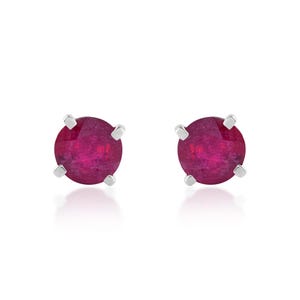 Puede incluir: Un par de pendientes de botón con gemas redondas de color rojo intenso. Cada gema está sujeta por cuatro garras plateadas, creando un diseño minimalista. Los pendientes se presentan sobre un fondo blanco.