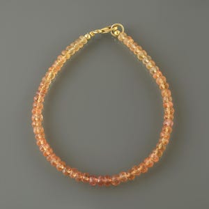 May include: A delicate bracelet composed of small, faceted, translucent orange-toned gemstone beads. The strand is secured with a polished gold-tone metal lobster claw clasp and a circular jump ring, creating a continuous circular loop design.