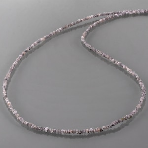 May include: A long necklace made of small, rough, grey diamonds. The necklace is laid out in a loose curve on a grey background.