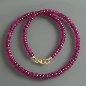 Puede incluir: Un collar compuesto por cuentas de rubí rosa oscuro facetadas. El collar está ensartado con un cierre dorado. Las cuentas son uniformes en tamaño y forma, creando un diseño continuo y elegante. El collar se muestra sobre un fondo gris.