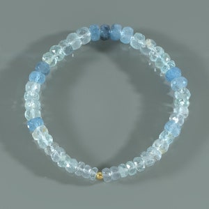 May include: A light blue aquamarine gemstone bracelet with a gold bead accent. The bracelet is made of round beads that are graduated in size, with the larger beads at the center of the bracelet.