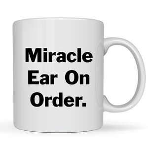 May include: White ceramic coffee mug with black text that reads "Miracle Ear On Order."