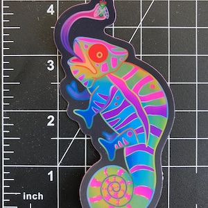 May include: A colorful chameleon sticker with a rainbow pattern and a green fly on its tongue. The chameleon is in a curled position with its tail curled around its body. The sticker is on a black grid background.