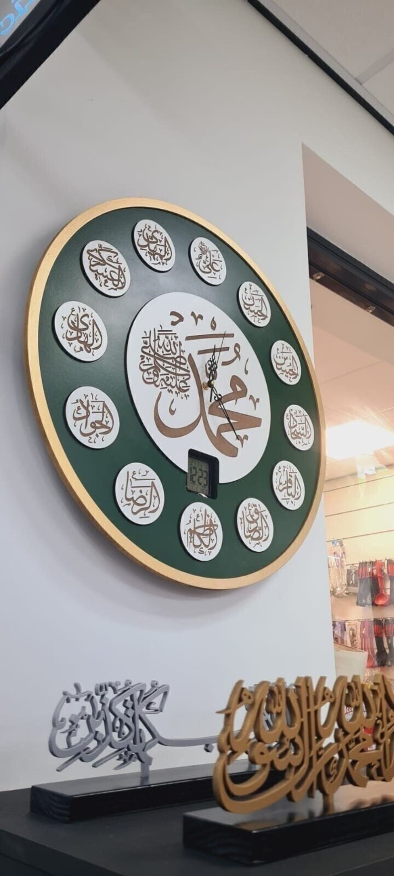 May include: A large, round, green and gold wall clock with Arabic calligraphy and a digital display showing the time 12:23. The clock is surrounded by smaller circles with Arabic calligraphy. There are two smaller decorative pieces with Arabic calligraphy on a black surface.