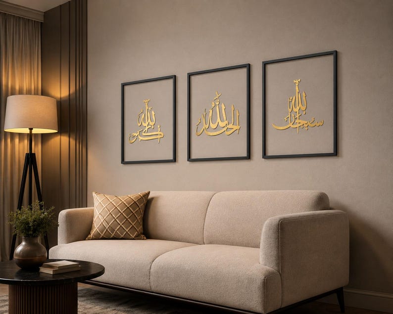 May include: Three framed gold Arabic calligraphy art pieces. Each piece features elegant script on a neutral background, set within black frames. The artwork hangs above a beige sofa with a patterned pillow, creating a warm and inviting living space.