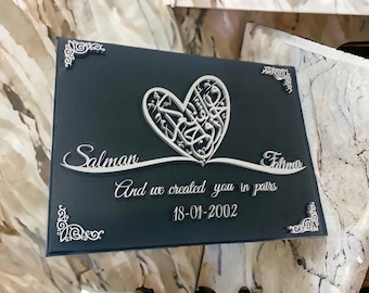 May include: A dark blue canvas with a white heart design featuring Arabic calligraphy. The names Salman and Fatima are written below the heart, along with the text "And we created you in pairs" and the date "18-01-2002".
