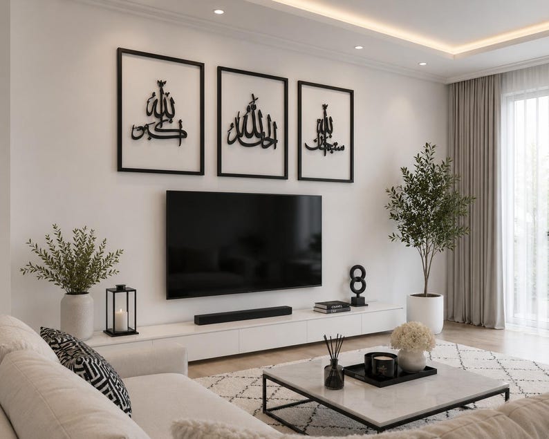 May include: A modern living room with a white sofa, a marble coffee table, and a large flat-screen TV. Three framed black and white Islamic calligraphy art pieces hang above the TV. Decorative plants and a black candle lantern add to the room's aesthetic.