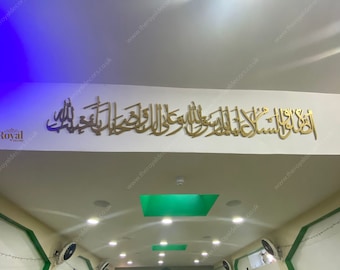 May include: A gold-coloured Islamic calligraphy wall art piece with the Arabic text "Allahumma salli ala Muhammad wa ala ali Muhammad" hanging on a white ceiling. The text translates to "O Allah, send blessings upon Muhammad and upon the family of Muhammad."