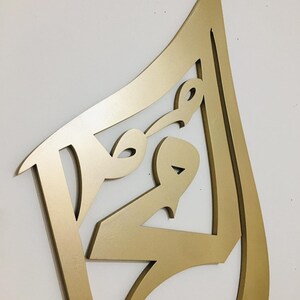 May include: Gold-colored metal wall art in the shape of an abstract design. The design is made of multiple overlapping curves and lines.
