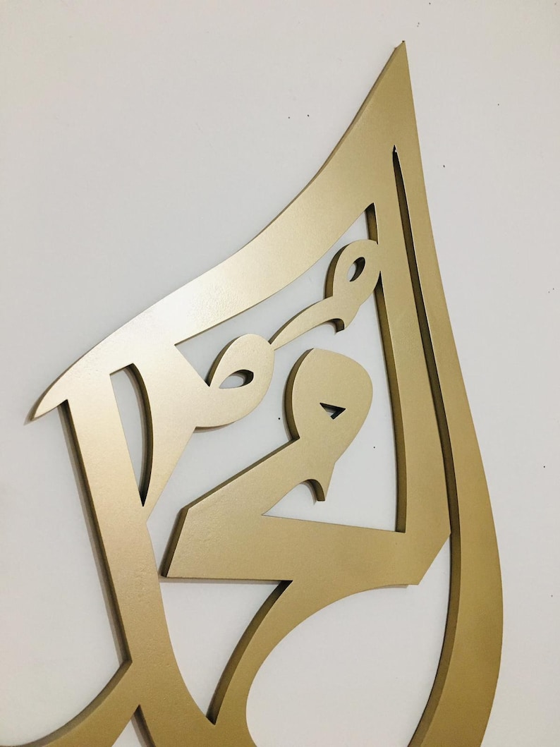 May include: Gold-colored metal wall art in the shape of an abstract design. The design is made of multiple overlapping curves and lines.