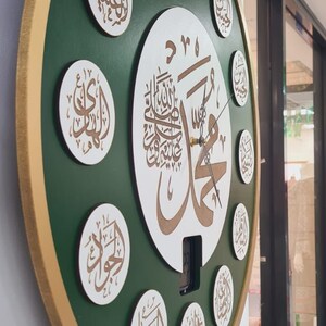 May include: A green and gold circular wall clock with Arabic calligraphy in white and gold. The clock has a white center with a large Arabic inscription and a smaller clock face with hands.