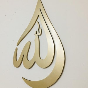May include: Gold-colored metal wall decor in the shape of a teardrop with the Arabic word "Allah" inscribed inside.